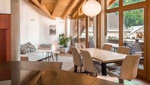Ein modernes Interieur mit Essbereich, einer Couch und großen Fenstern mit Blick ins Freie.