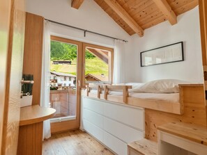 A room with a wooden ceiling, a bed with a wooden headboard, a window with a view of buildings, and a framed picture on the wall.