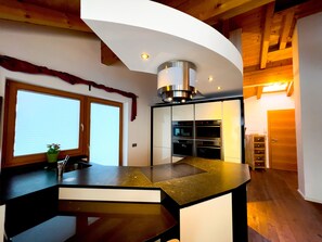 A modern kitchen with a curved island, built-in ovens, and a wooden ceiling.