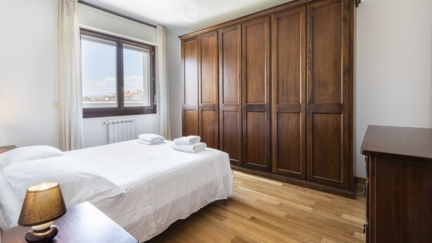 A bedroom with a bed, a nightstand, a wooden wardrobe, and a window with curtains.