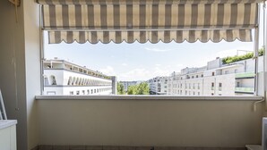 A balcony with a striped awning, a tiled floor, and a view of buildings in the distance.