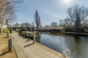 A riverside walkway with a bridge, a green boat docked, and a calm water body reflecting the sky.