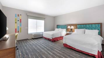 Habitación de hotel con dos camas, un escritorio, una silla y un ventanal grande.