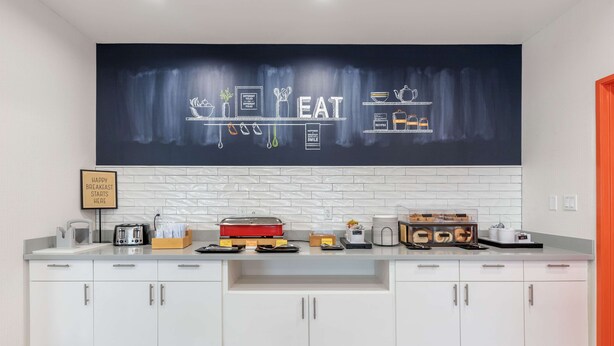 Eine moderne Küche mit weißen Schränken, einer schwarzen Spritzschutzwand und einer großen Tafel, auf der Küchenutensilien und das Wort "EAT" abgebildet sind.
