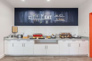 A modern kitchen with white cabinets, a black backsplash, and a large chalkboard wall with kitchen utensils and the word "EAT".