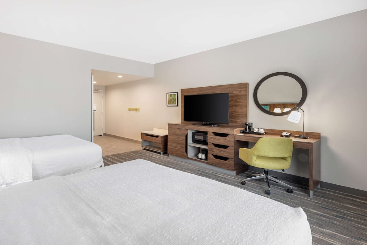 A hotel room with two beds, a desk with a chair, a television, and a mirror.