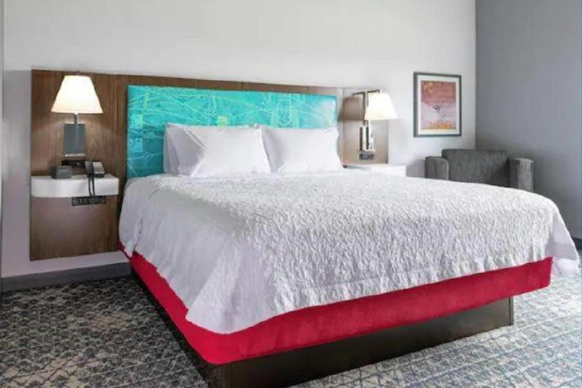 A hotel room with a bed, two bedside lamps, a nightstand, a chair, and a wall-mounted painting.