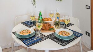 A dining table with plates of food, glasses, and bottles, surrounded by white chairs. - Mandorli 1/18 Apartment by Wonderful Italy (Desenzano del Garda)