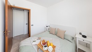 A bedroom with a bed, bedside table, and a tray with breakfast items. - Mandorli 1/18 Apartment by Wonderful Italy (Desenzano del Garda)