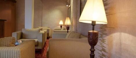 A hotel lounge with sofas and armchairs, a patterned carpet, and wall-mounted lamps.