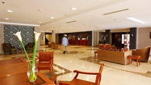 Un vestíbulo de hotel con mostrador de recepción, zona de estar y un jarrón con flores.