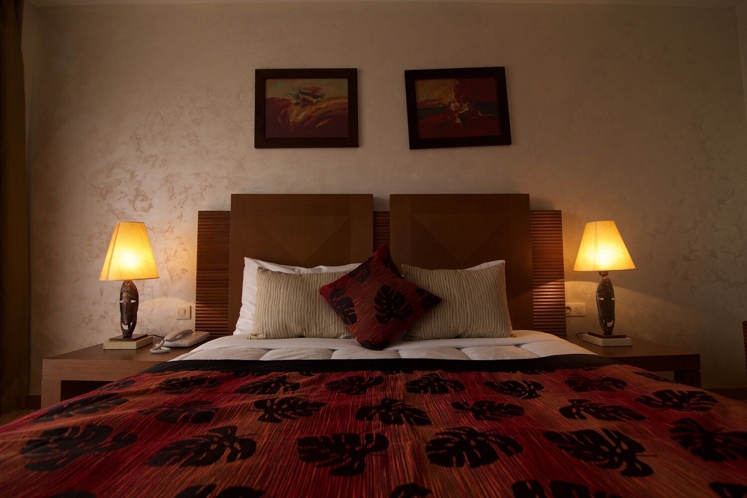 A hotel room with a large bed, two bedside lamps, a headboard, and two framed artworks on the wall.