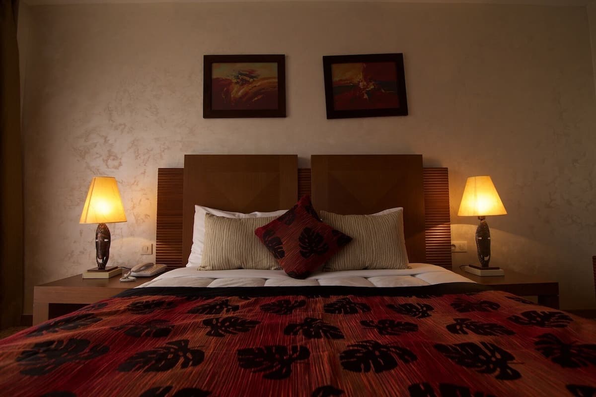 A hotel room with a large bed, two bedside lamps, a headboard, and two framed artworks on the wall.