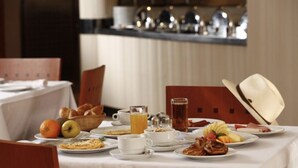Un desayuno con una variedad de platos, entre ellos frutas, pastelería y bebidas, sobre una mesa con mantel blanco.