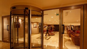 Un vestíbulo de hotel con puerta giratoria, una zona de estar con sofás y un suelo de mármol pulido.
