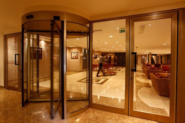A hotel lobby with a revolving door, a seating area with sofas, and a polished marble floor. - Hala Hotel & Aqua Park (Bissau)