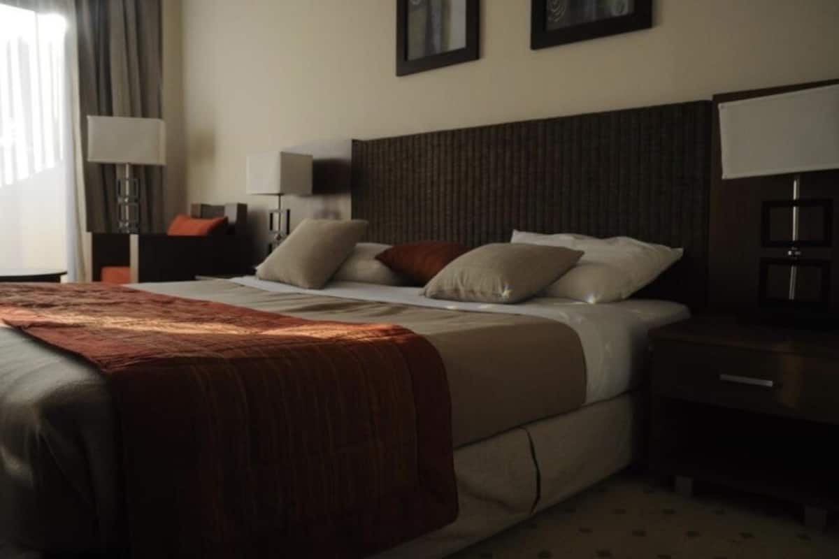 A hotel room with a large bed, a nightstand, a lamp, and a window with curtains.