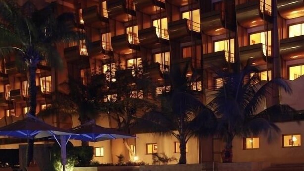Vista nocturna de un hotel con piscina, palmeras y balcones iluminados.