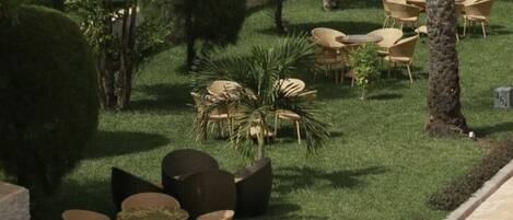 Een terras met ronde tafels en stoelen, omringd door een verzorgd gazon en bomen.