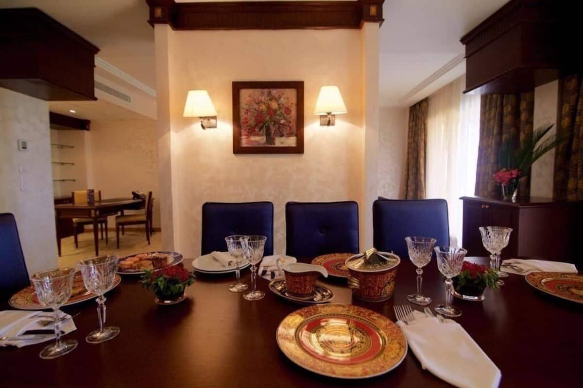 A formal dining room with a long table set for a meal, two wall-mounted lamps, and a framed floral painting above the table.