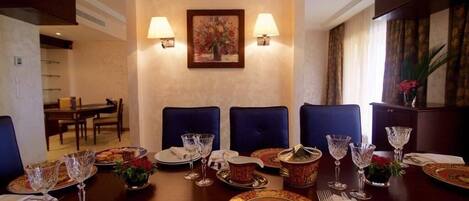 A formal dining room with a long table set for a meal, two wall-mounted lamps, and a framed floral painting above the table.