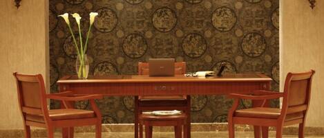 A dining area with a long wooden table, four chairs, a vase with flowers, and a laptop.