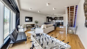 A modern living room with a foosball table, a sofa, and a kitchen in the background. - Modern 4 Story Townhome -5 minutes walk to Deep Ellum & Fair Park! (Dallas)