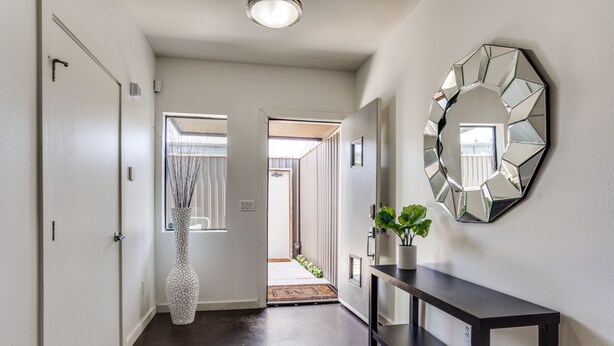 A hallway with a dark wooden floor, a white door, a large mirror, and a console table with a potted plant. - Modern 4 Story Townhome -5 minutes walk to Deep Ellum & Fair Park! (Dallas)