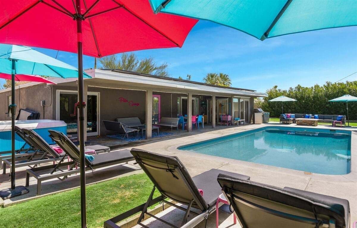 A pool area with lounge chairs and umbrellas, a covered patio, and a building with a sign that reads "Poolside Cafe."