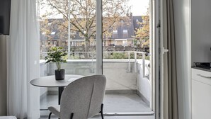 A modern hotel room with a balcony, a dining table with a chair, a potted plant, and a flat-screen TV mounted on the wall. - MOOI Apartments Grenchen (Grenchen)