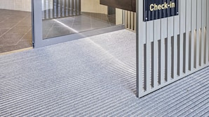 A self-check-in area with a glass partition, a reception desk, and a sign indicating self-service. - MOOI Apartments Grenchen (Grenchen)