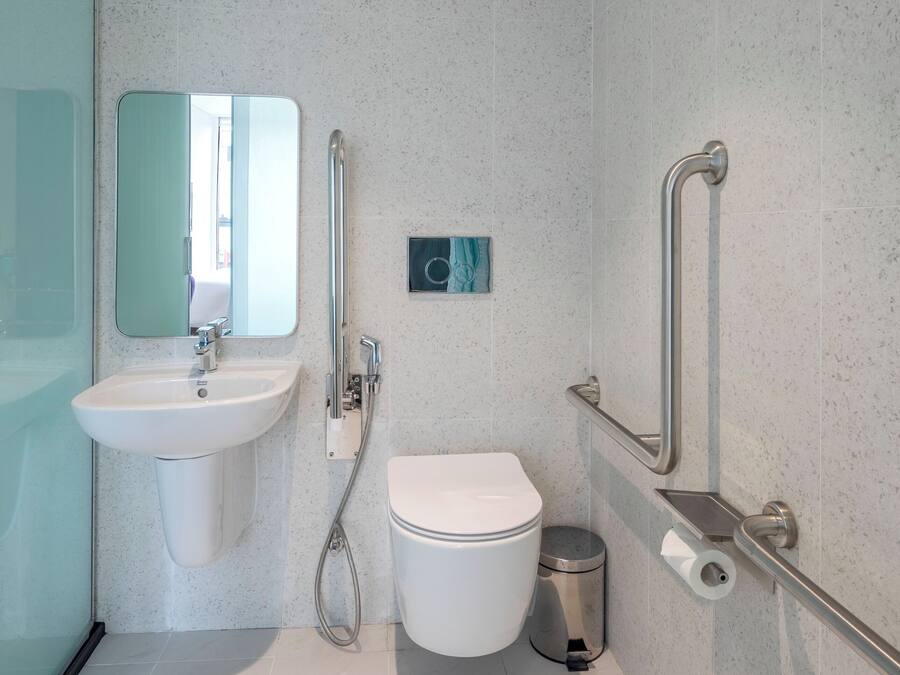 Une salle de bain moderne avec un lavabo, des toilettes et des barres d’appui, le tout de couleur blanche.