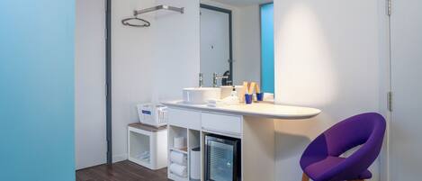 A modern bathroom with a white vanity, a built-in refrigerator, a purple chair, and a large mirror.