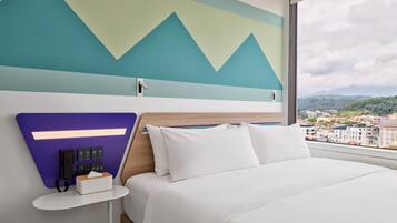 Una habitación de hotel moderna con una cama, una mesita de noche, un teléfono en la pared y un ventanal con vistas a la ciudad.