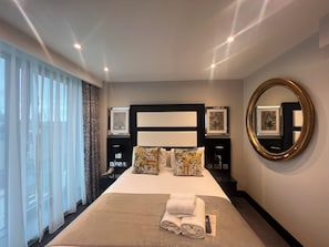 A hotel room with a large bed, a round mirror, and a window with sheer curtains. - Hatton Garden Hotel (London)