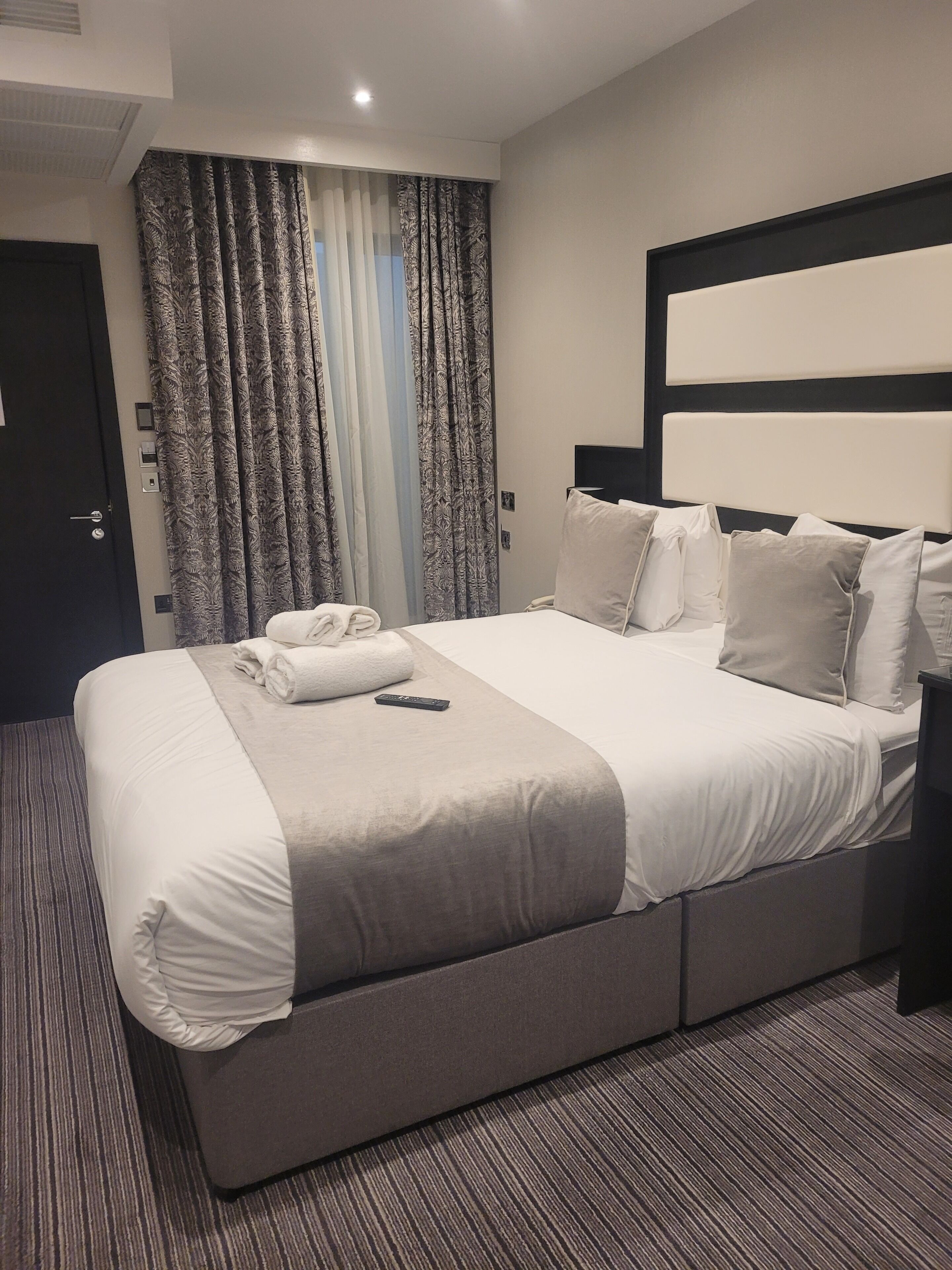 A neatly made bed with white linens, a remote control, and a folded towel on the bed.