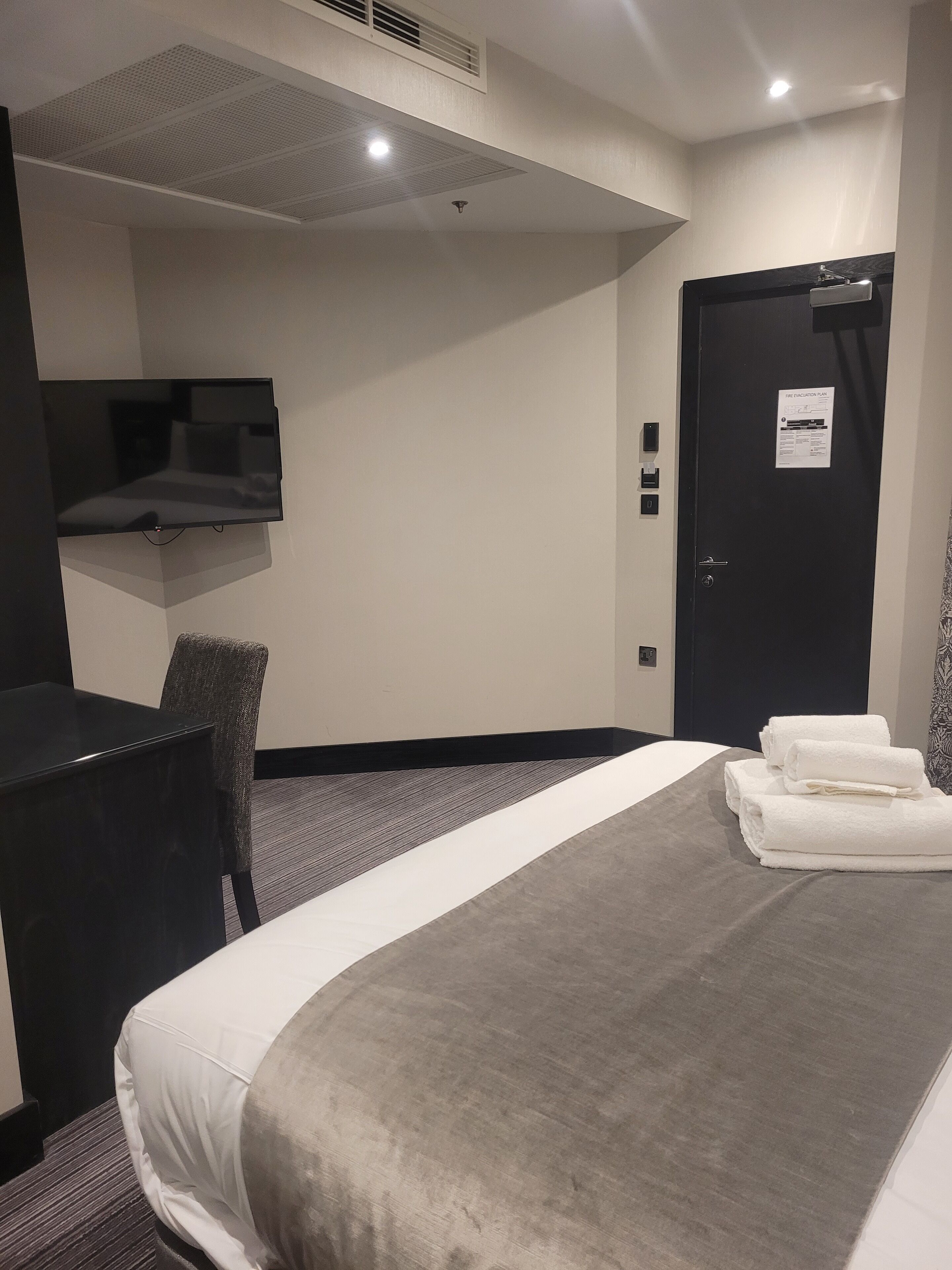 Habitación de hotel con cama, escritorio, silla, televisor de pantalla plana y puerta con un cartel.