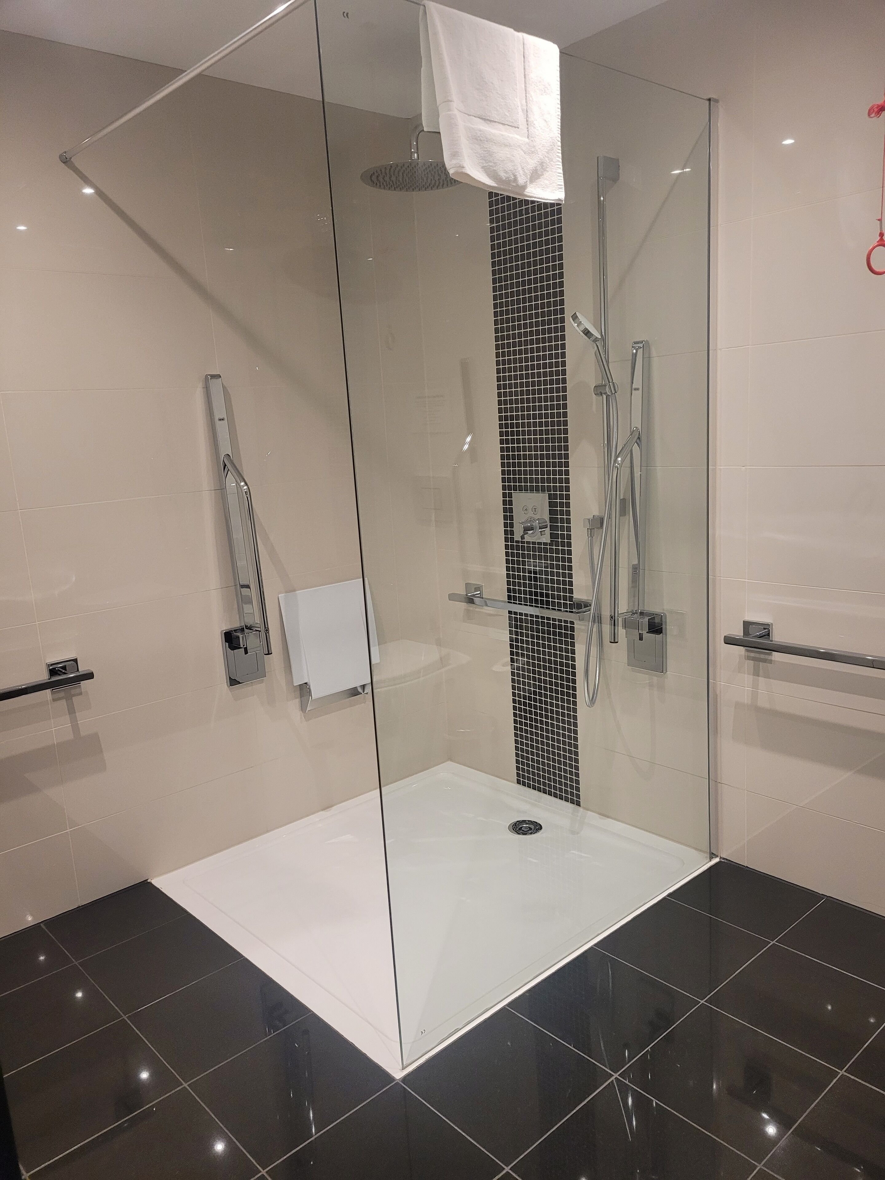 Un baño moderno con ducha envuelta en vidrio, una toalla blanca colgada y una pared decorativa con mosaicos blanco y negro.