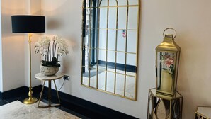 A hallway with a large arched mirror, a floor lamp, a small table with flowers, and a lantern. - Hatton Garden Hotel (London)