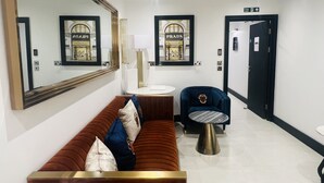 A hotel lobby with a brown sofa, a round table, and a mirror reflecting a Prada store sign. - Hatton Garden Hotel (London)