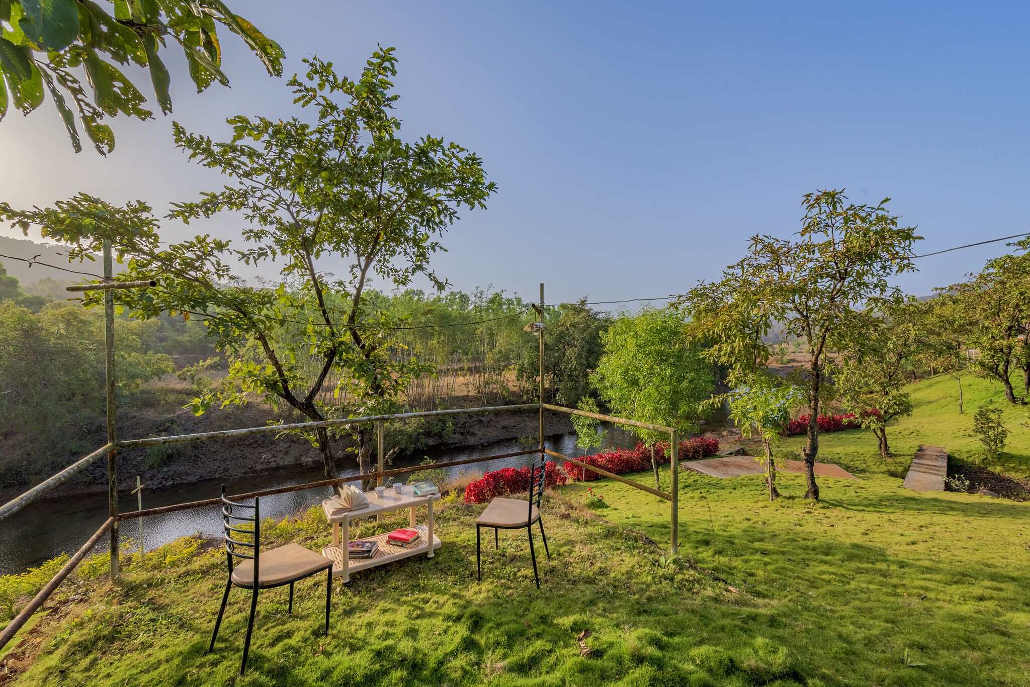 A serene outdoor seating area with a table and chairs, overlooking a river and lush greenery.