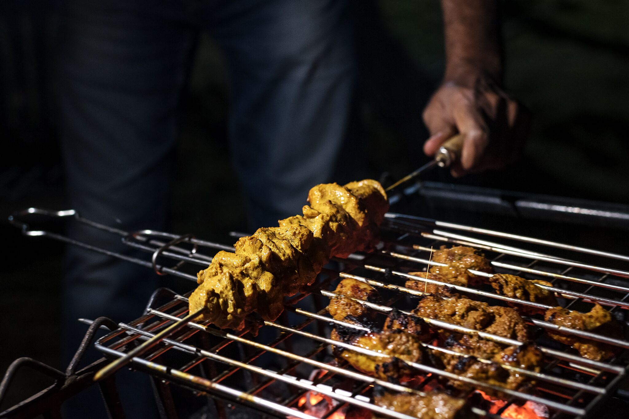 En person griller spyd med kød på en grill.