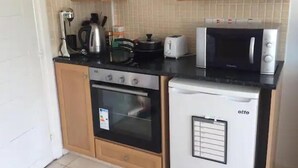 A compact kitchen with wooden cabinets, a stove, a microwave, and a small refrigerator.