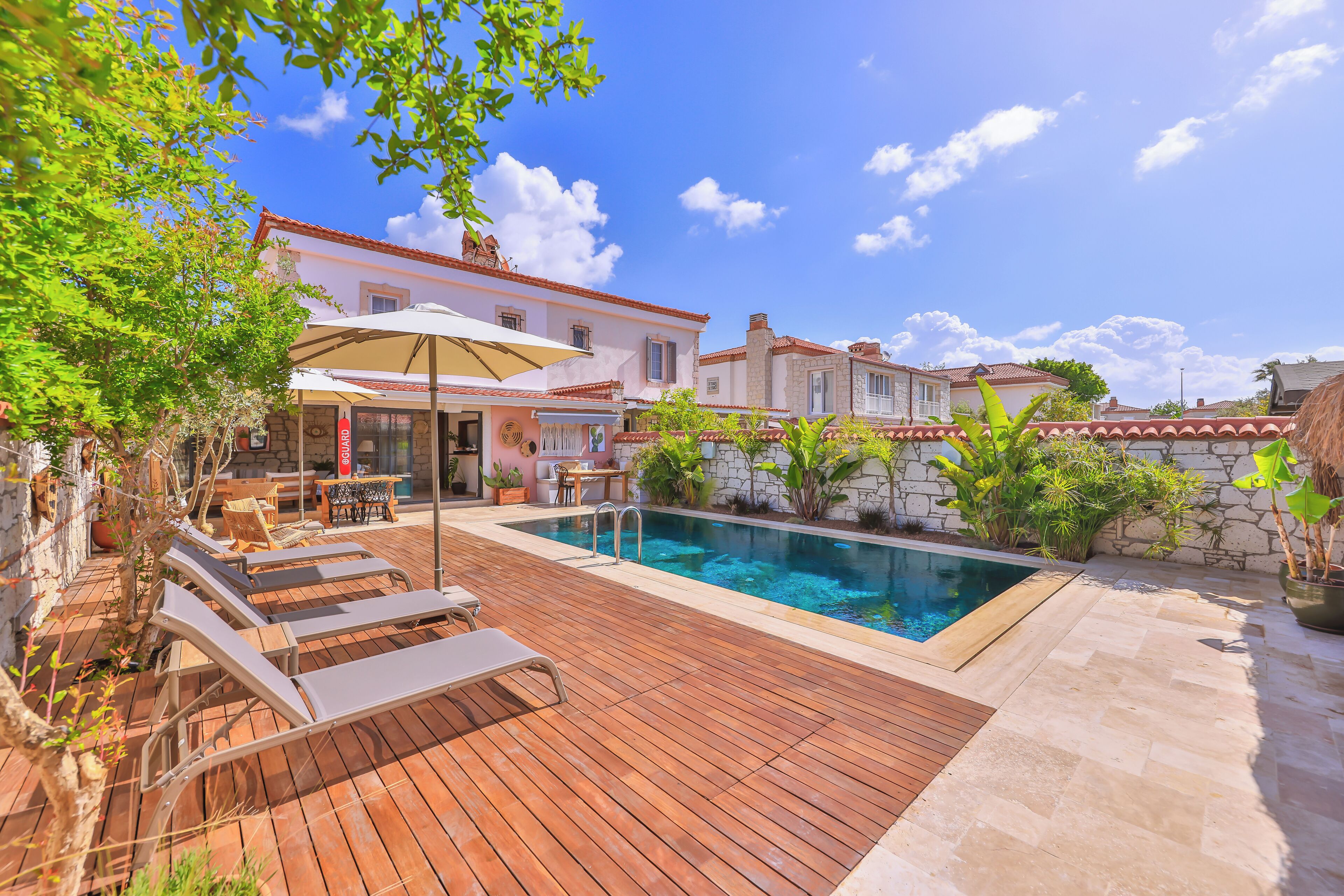 A pool area with wooden decking, lounge chairs, and a table with umbrellas.