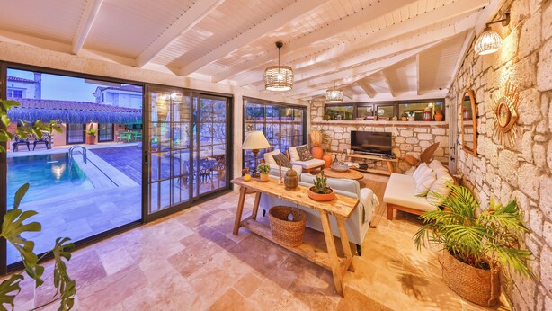 A spacious living area with a pool view, a stone fireplace, and comfortable seating. - Caliza Alacati (Cesme)