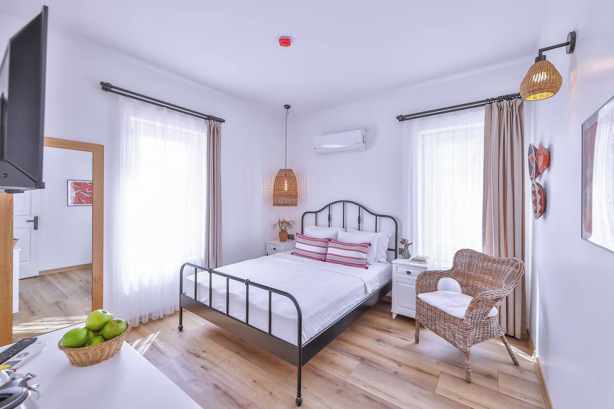 A modern bedroom with a bed, bedside tables, a wicker chair, and a TV.
