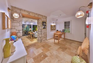 A spacious room with a stone accent wall, a dining area with a table and chairs, and a view of a garden through a window. - Caliza Alacati (Cesme)