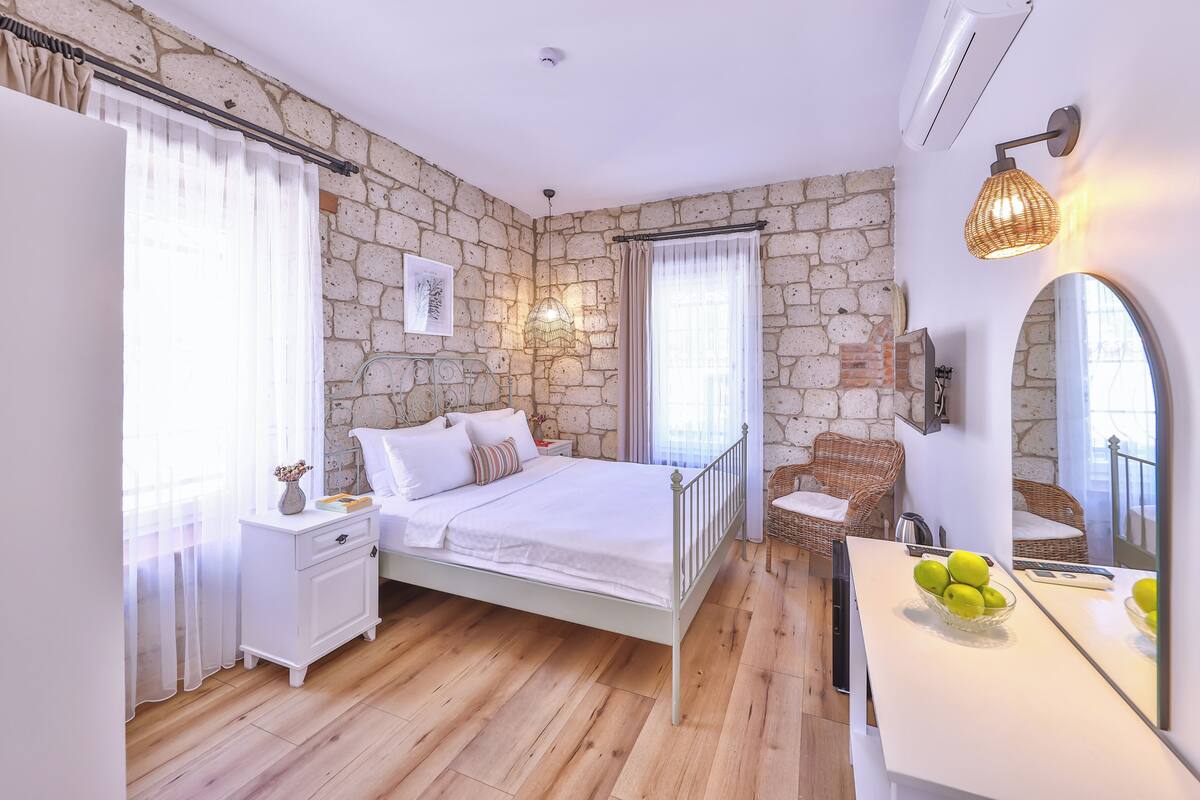 A bedroom with a stone wall, a bed, a bedside table, a chair, and a mirror.