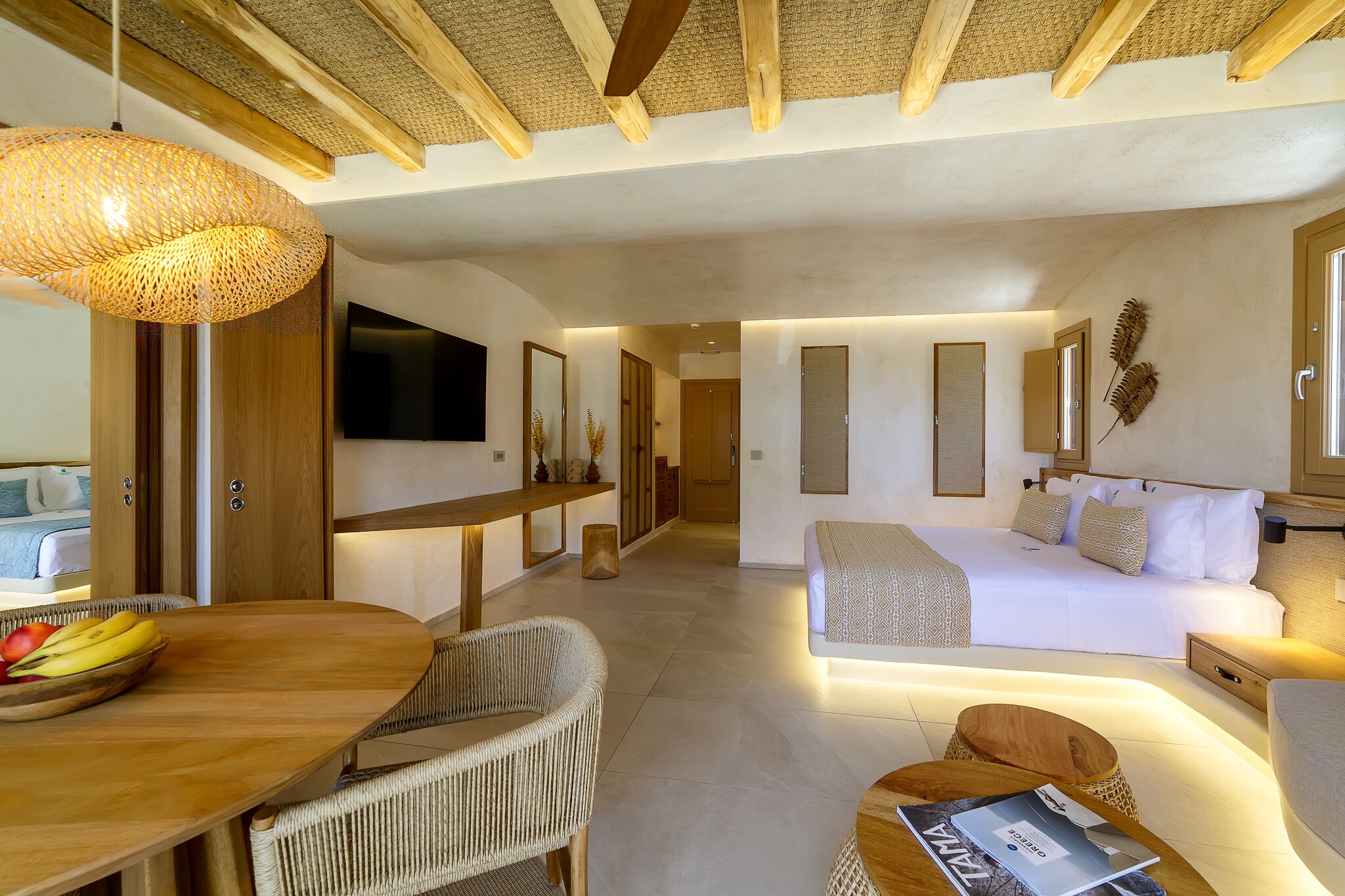 Una habitación de hotel moderna con una cama grande, un área de comedor con mesa y sillas, y un televisor montado en la pared.