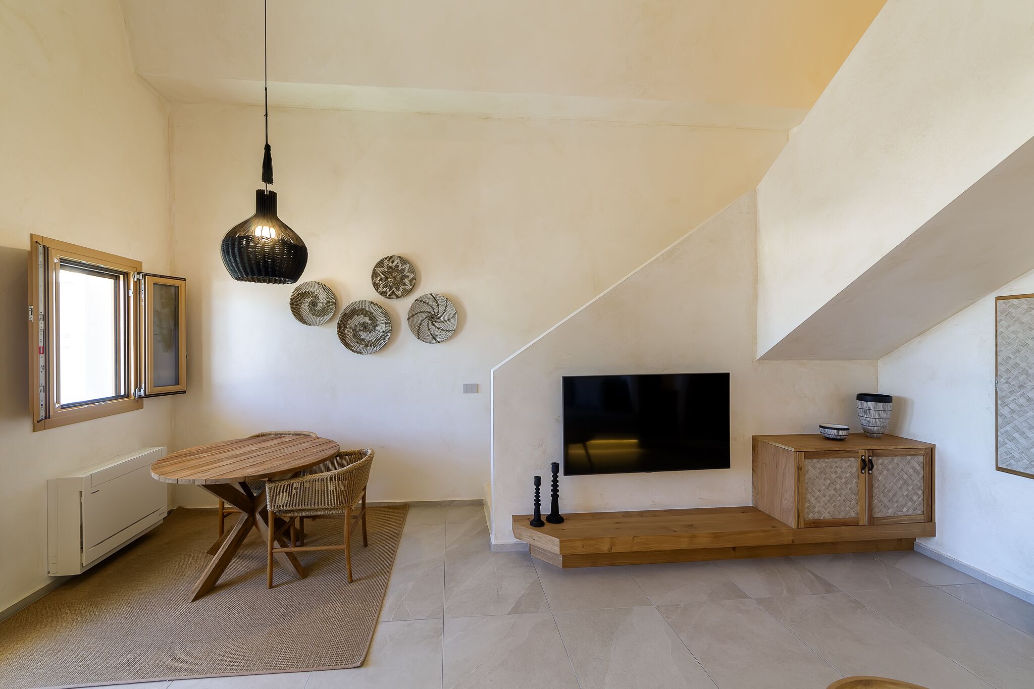 A modern living room with a dining table, chairs, a TV, and decorative plates on the wall.